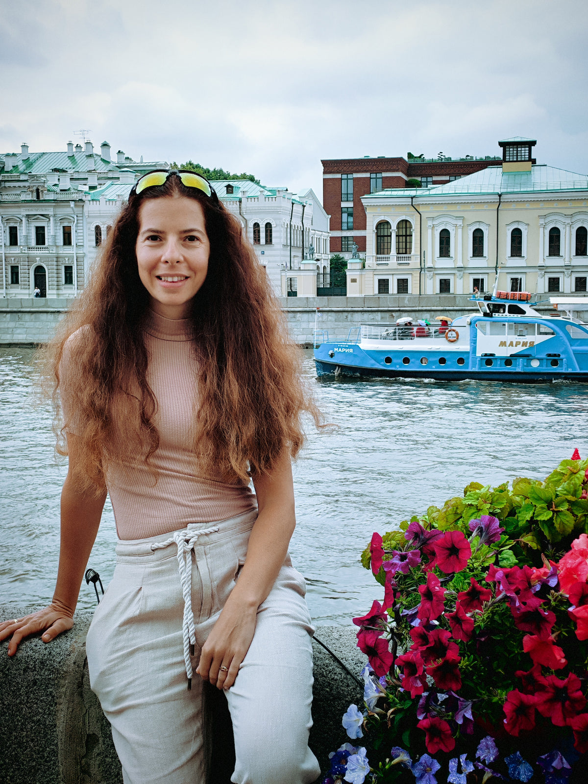 Szandi a Moszkva folyó partján, virágokkal és városi épületekkel a háttérben.
