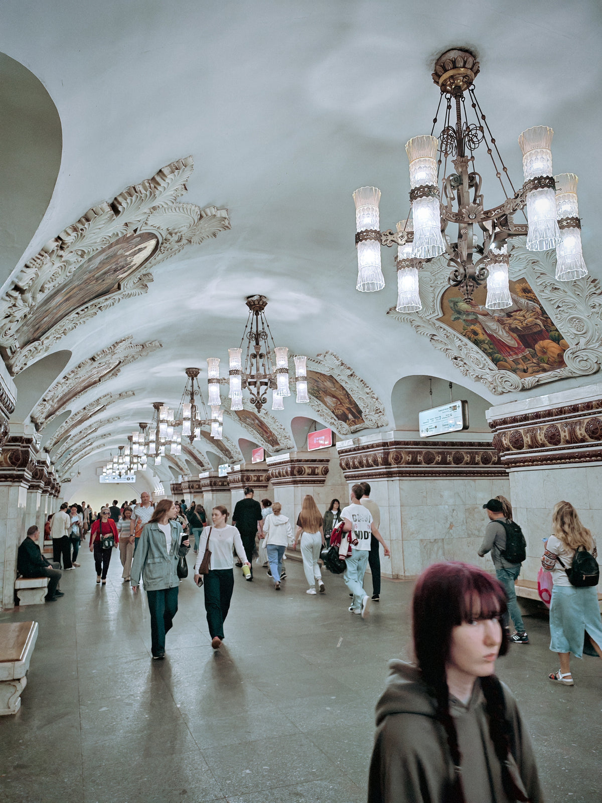Gazdagon díszített, boltozatos moszkvai metróállomás utasokkal.