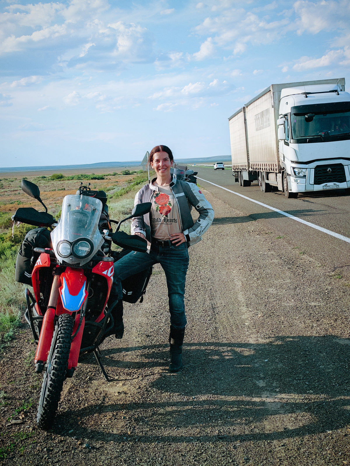 Szandi a Honda CRF 300 Rally mellett, háttérben egy elhaladó kamionnal Kazahsztánban.