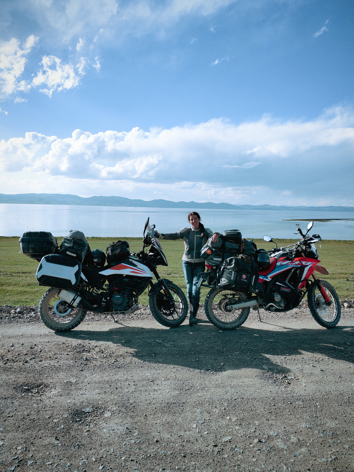 A Honda CRF 300 Rally és a KTM 390 Adventure a Song-Köl partján, a tóval és a hegyekkel a háttérben.