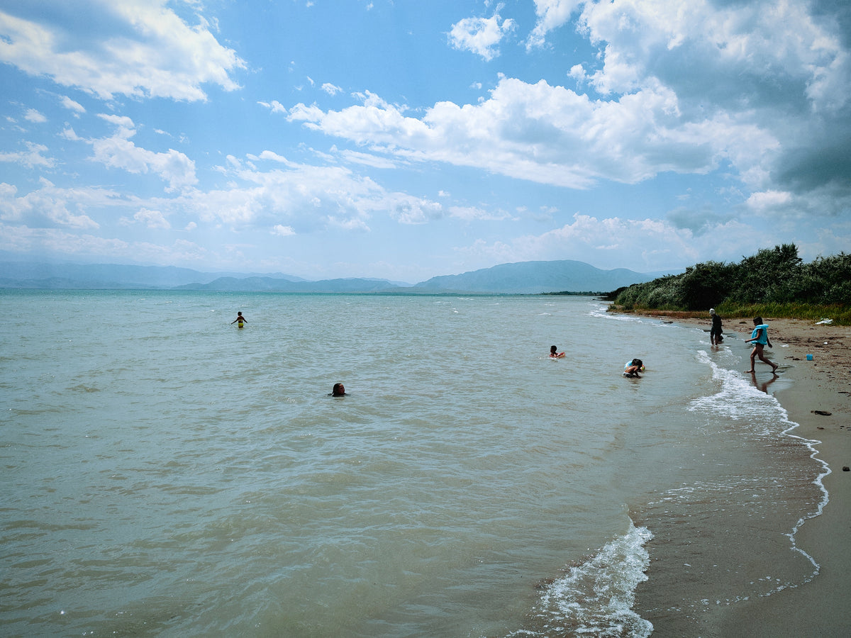 Fürdőzők az Issyk-Kul vizében, hegyekkel a háttérben.