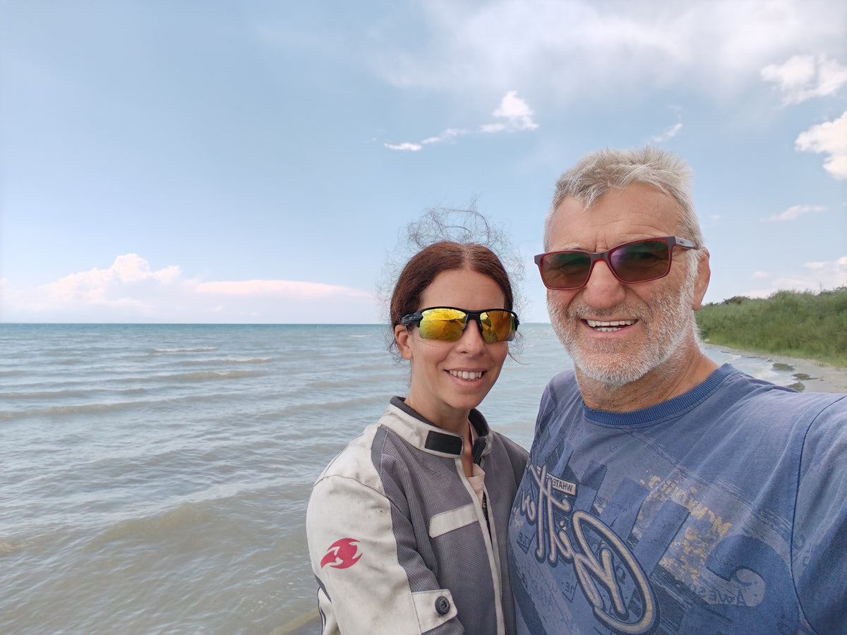 Szandi és Laci az Issyk-Kul partján, mögöttük a kék tó és a hegyek.