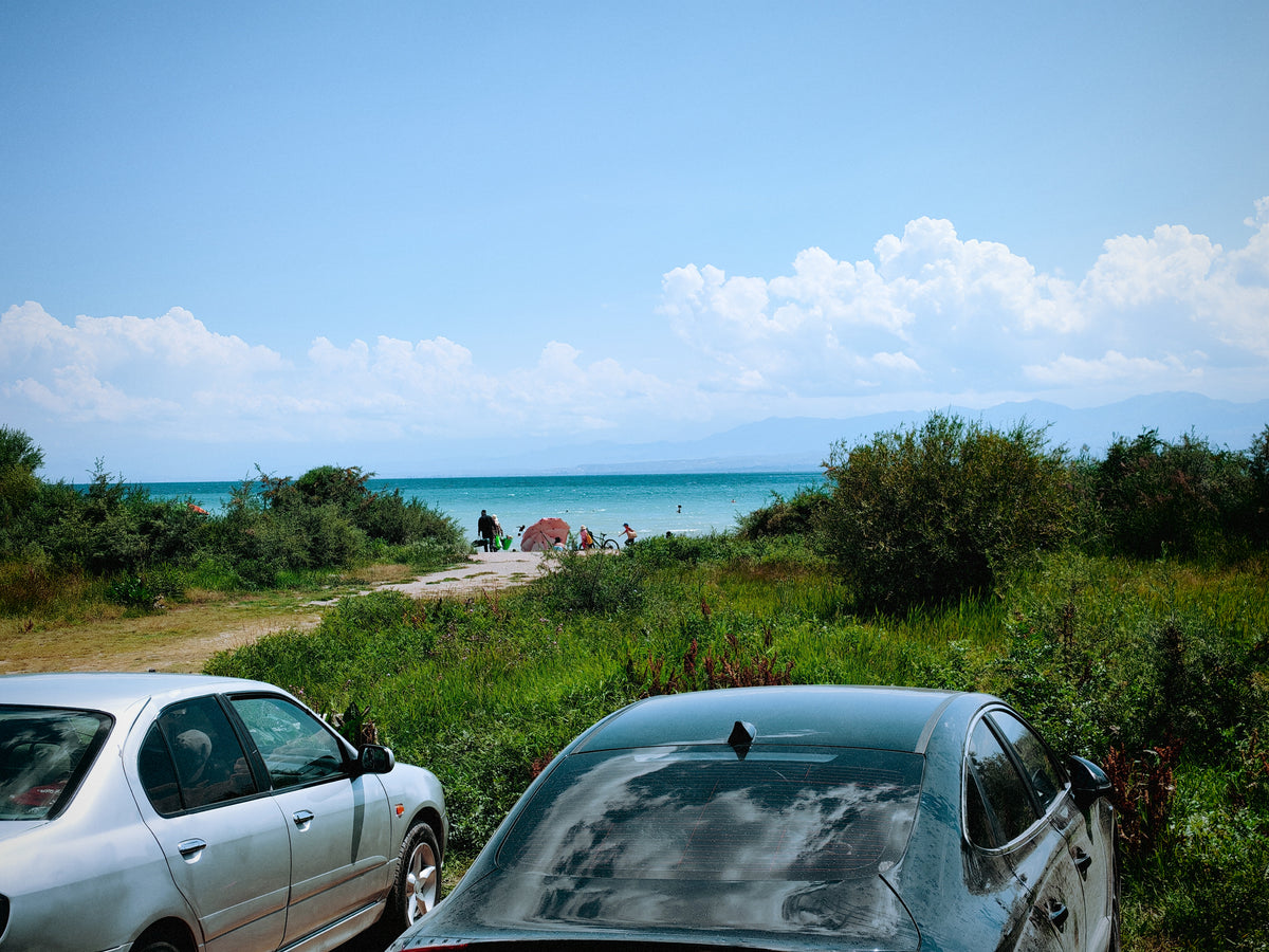 Autók az Issyk-Kul partján, háttérben a tóval és a hegyekkel.